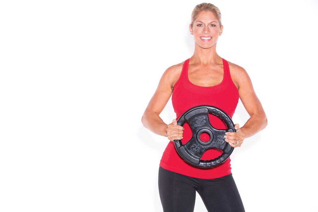Woman in a red workout top holding a weight plate at her waist.