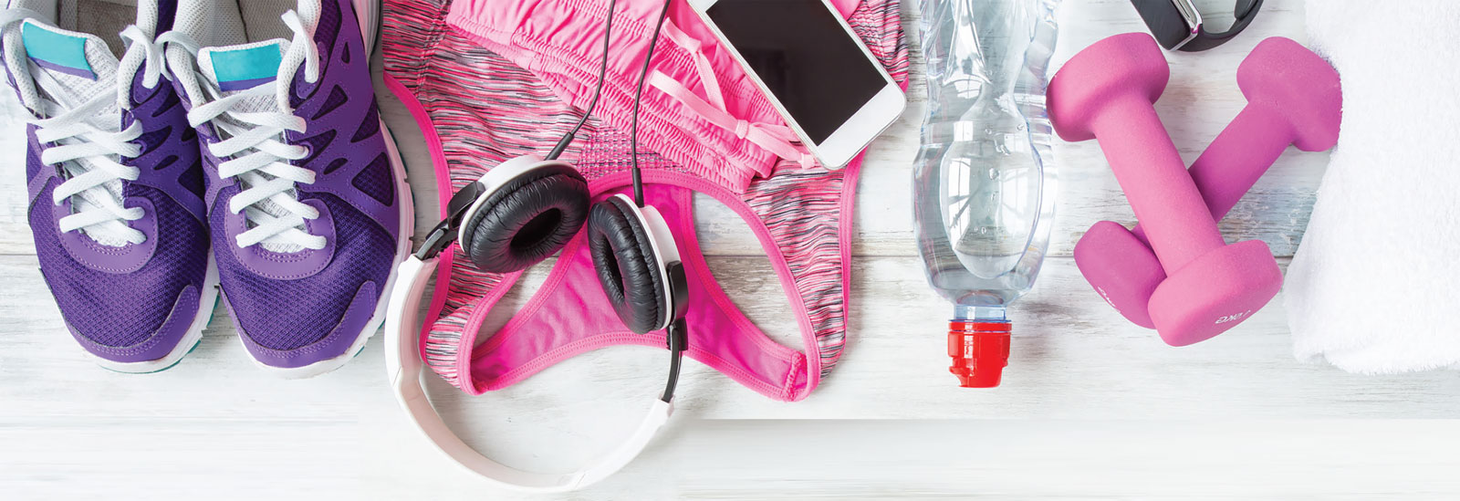 Workout essentials including trainers, headphones, a phone, water bottle and pink dumbbells.