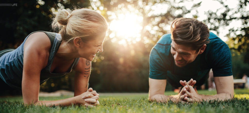 Two people holding forearm planks beside each other on grass outdoors.