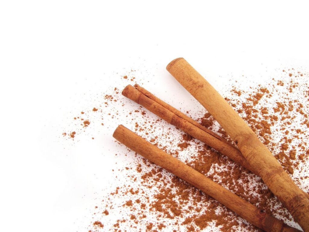 Three cinnamon sticks lying on a white surface with ground cinnamon sprinkled around them.