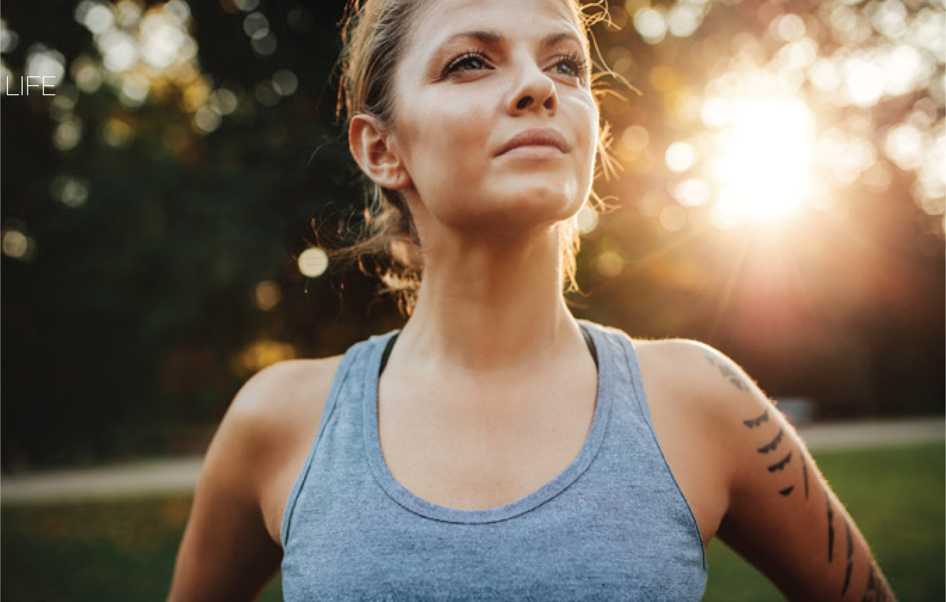 Woman in a grey athletic top outdoors in warm evening light.