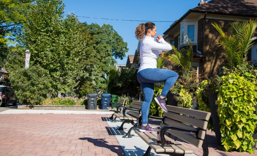 Woman stepping onto a park bench and lifting one knee.