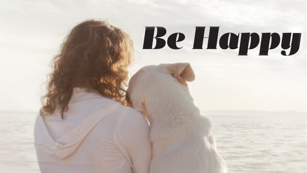 Person holding a small dog by the sea beneath the heading Be Happy.