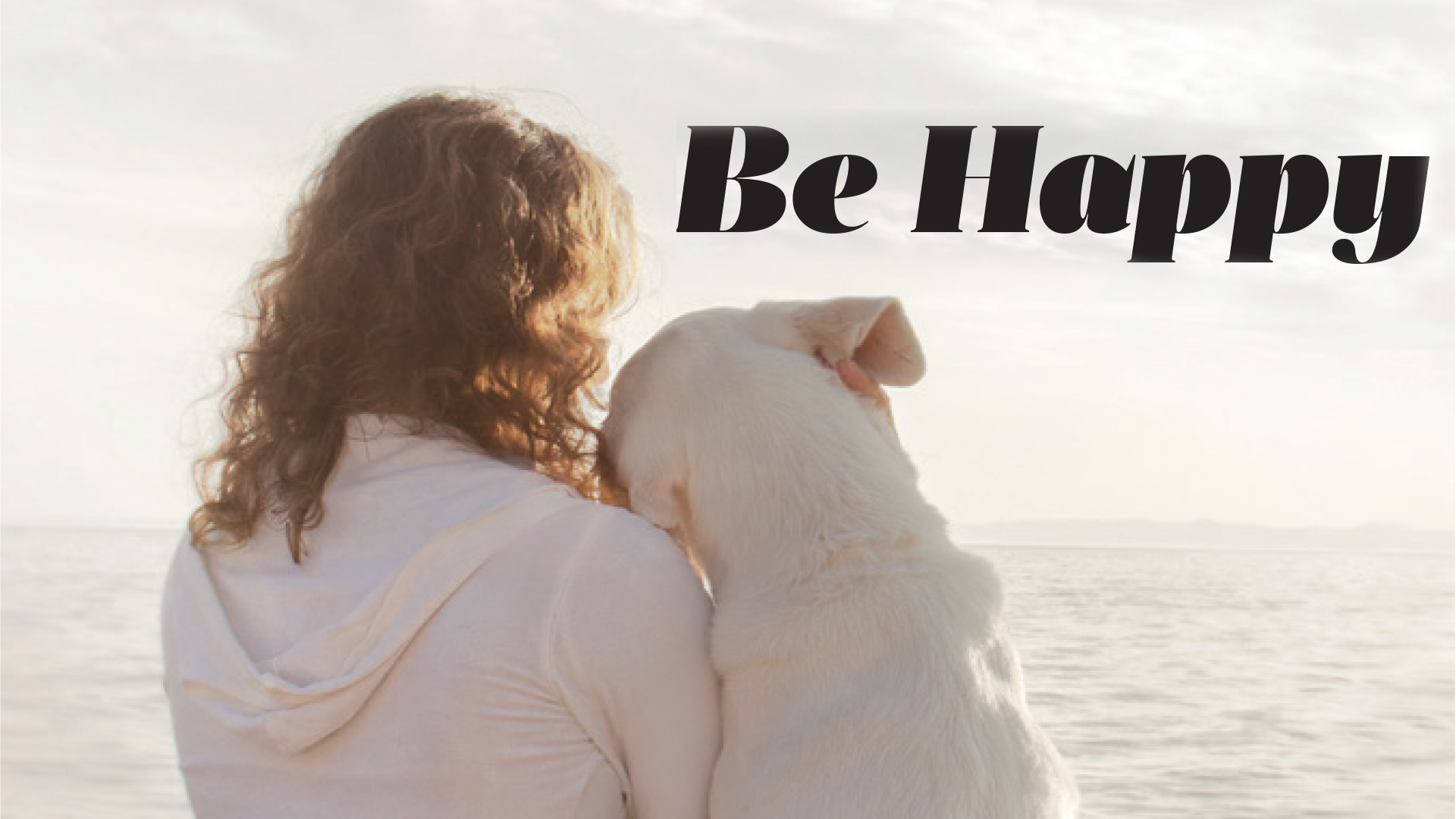 Person holding a small dog by the sea beneath the heading Be Happy.