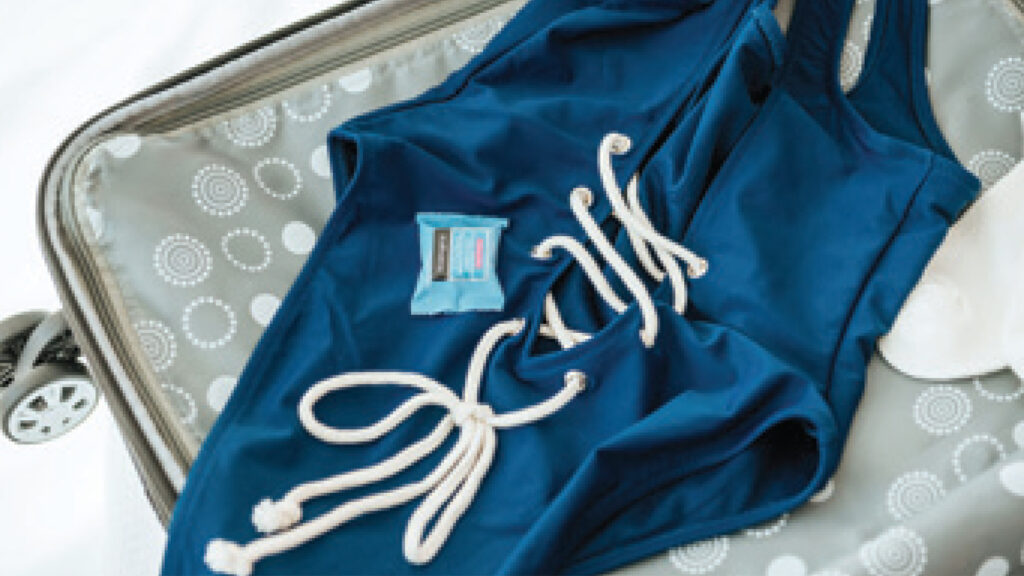 Blue swimsuit with white lace-up detailing packed in an open suitcase.