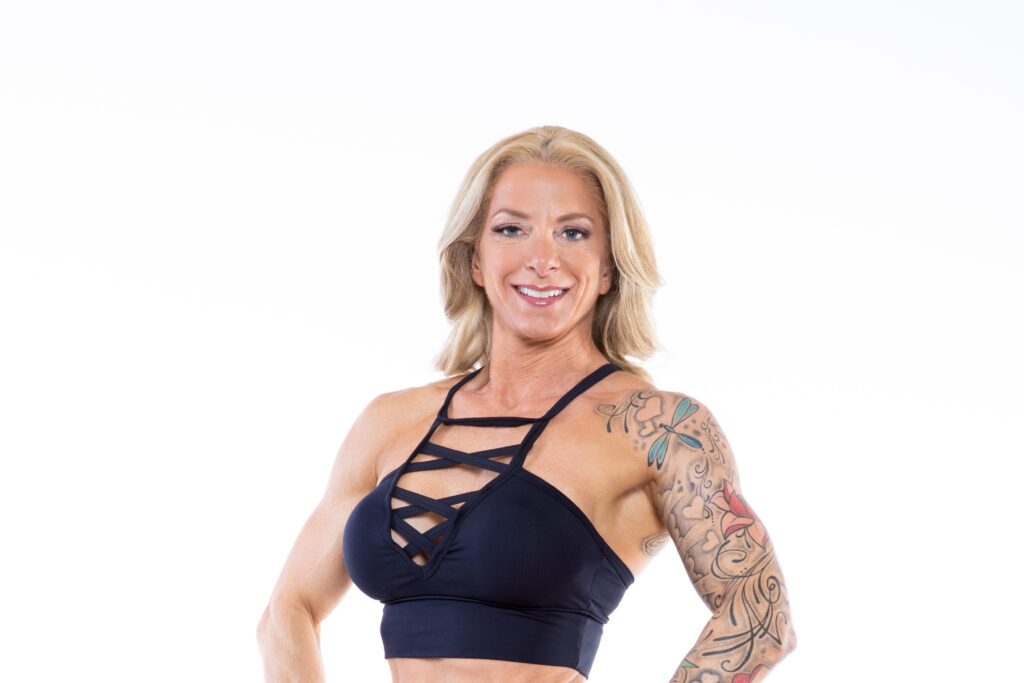Smiling woman with an arm tattoo wearing a black strappy sports bra.