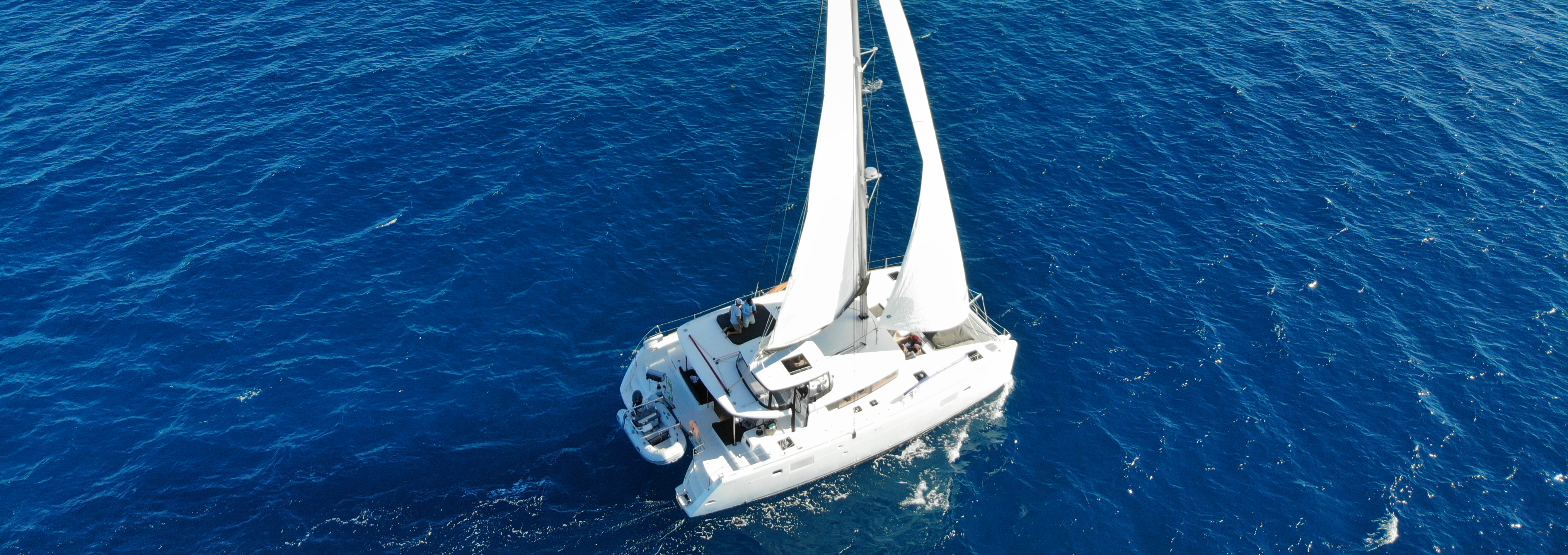 Aerial view of a white sailing catamaran on deep blue water.