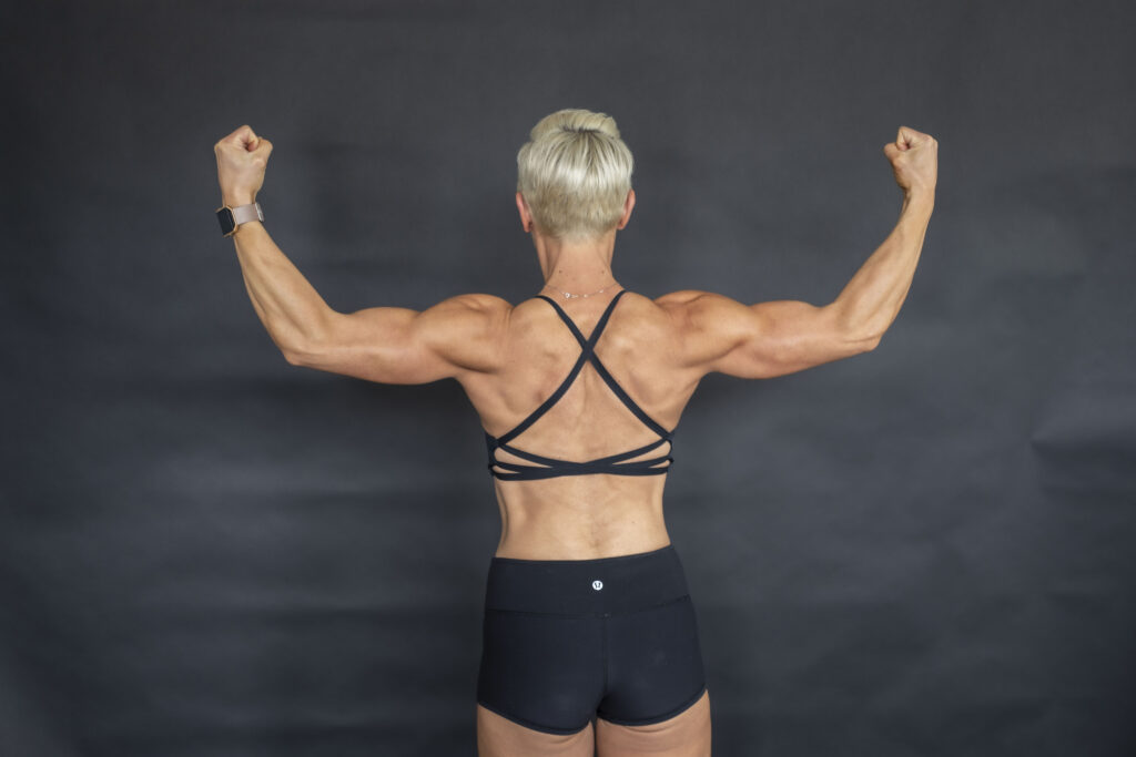 Rear view of a woman in a black workout outfit flexing both arms.