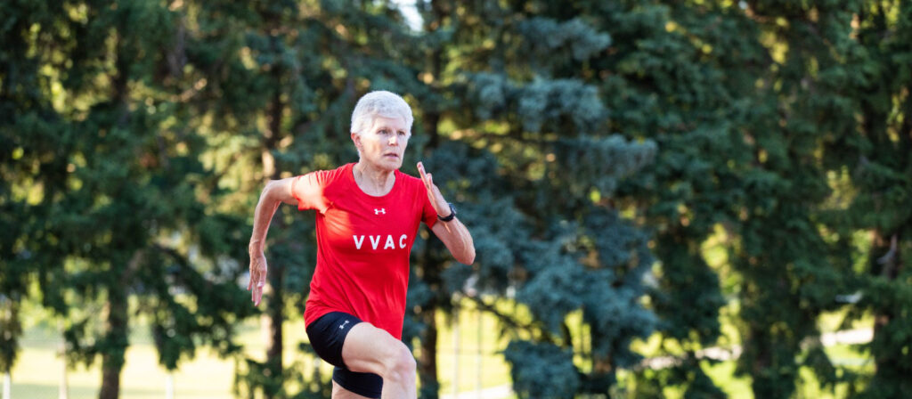 Runner in a red sleeveless top and headband exercising outdoors near trees.