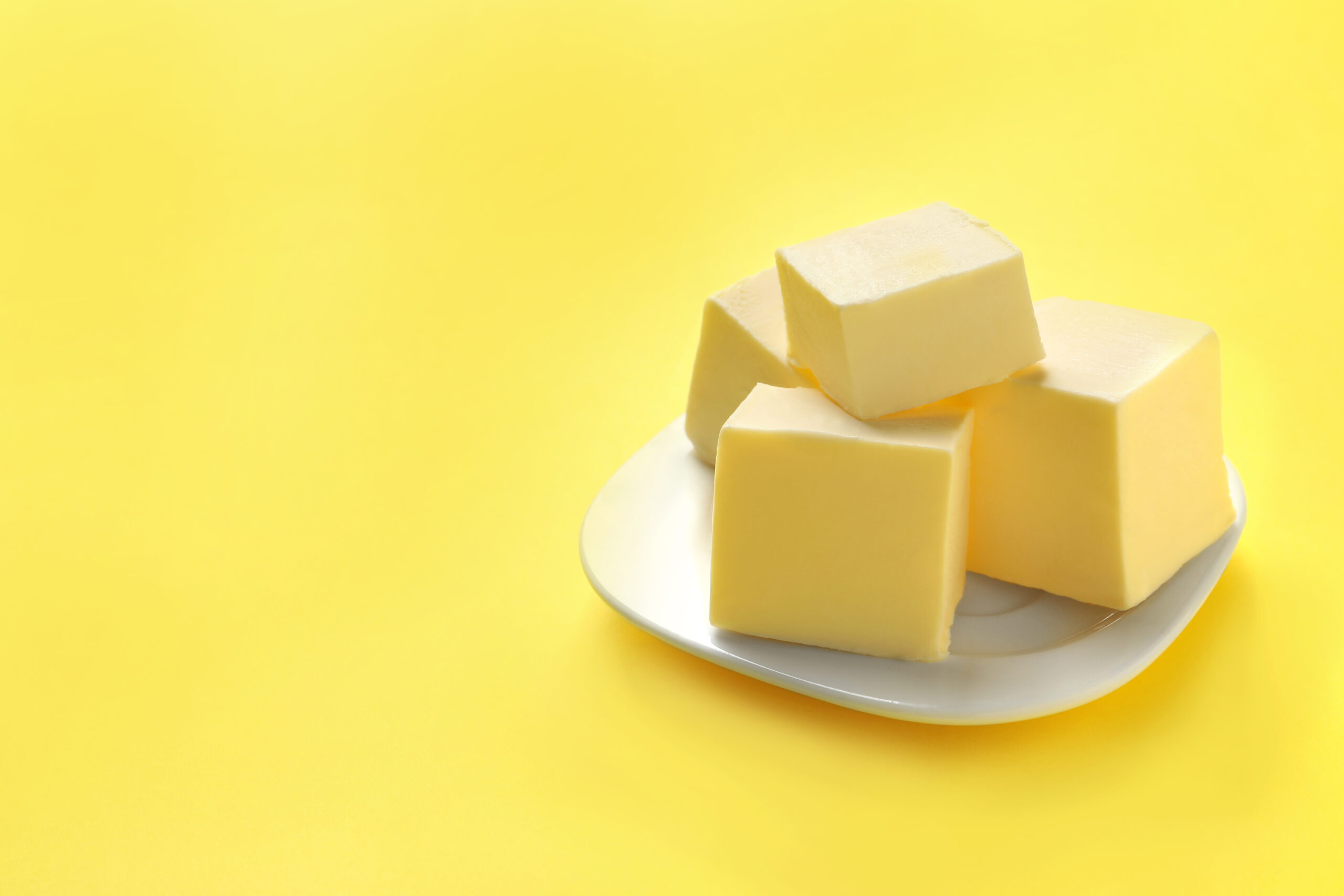Blocks of butter on a white plate against a yellow background.
