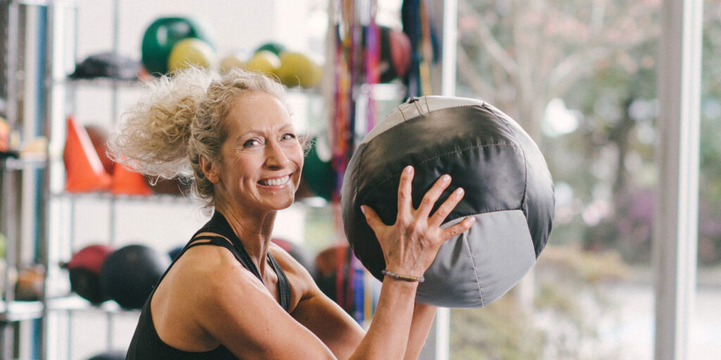 Smiling woman holding a large medicine ball in a gym.