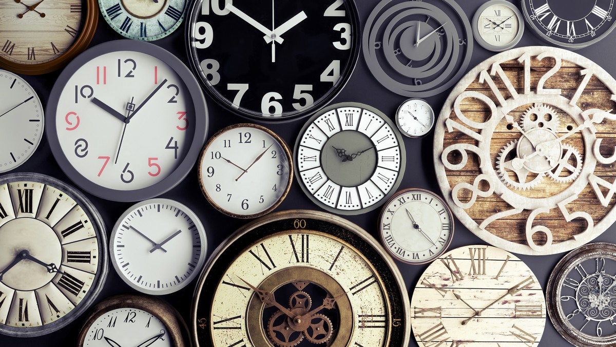 A collection of various wall clocks with different designs and times, arranged closely together on a dark background.