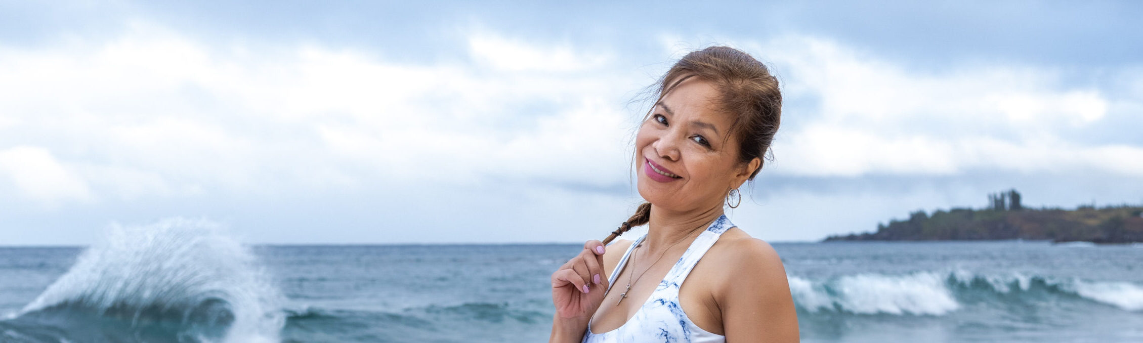Smiling woman standing on a beach with ocean waves behind her.