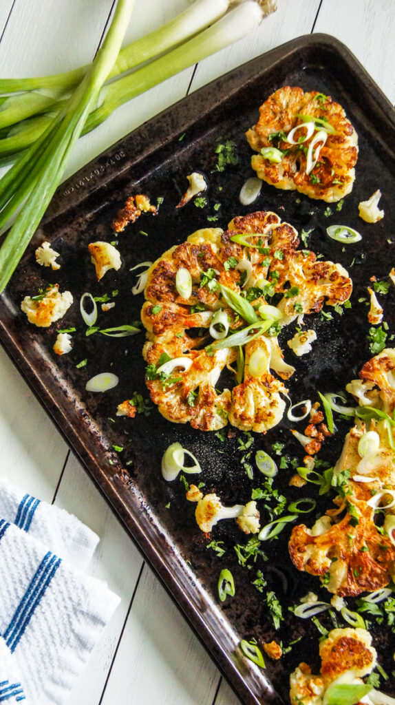 Roasted cauliflower steaks garnished with sliced green onions on a baking tray.