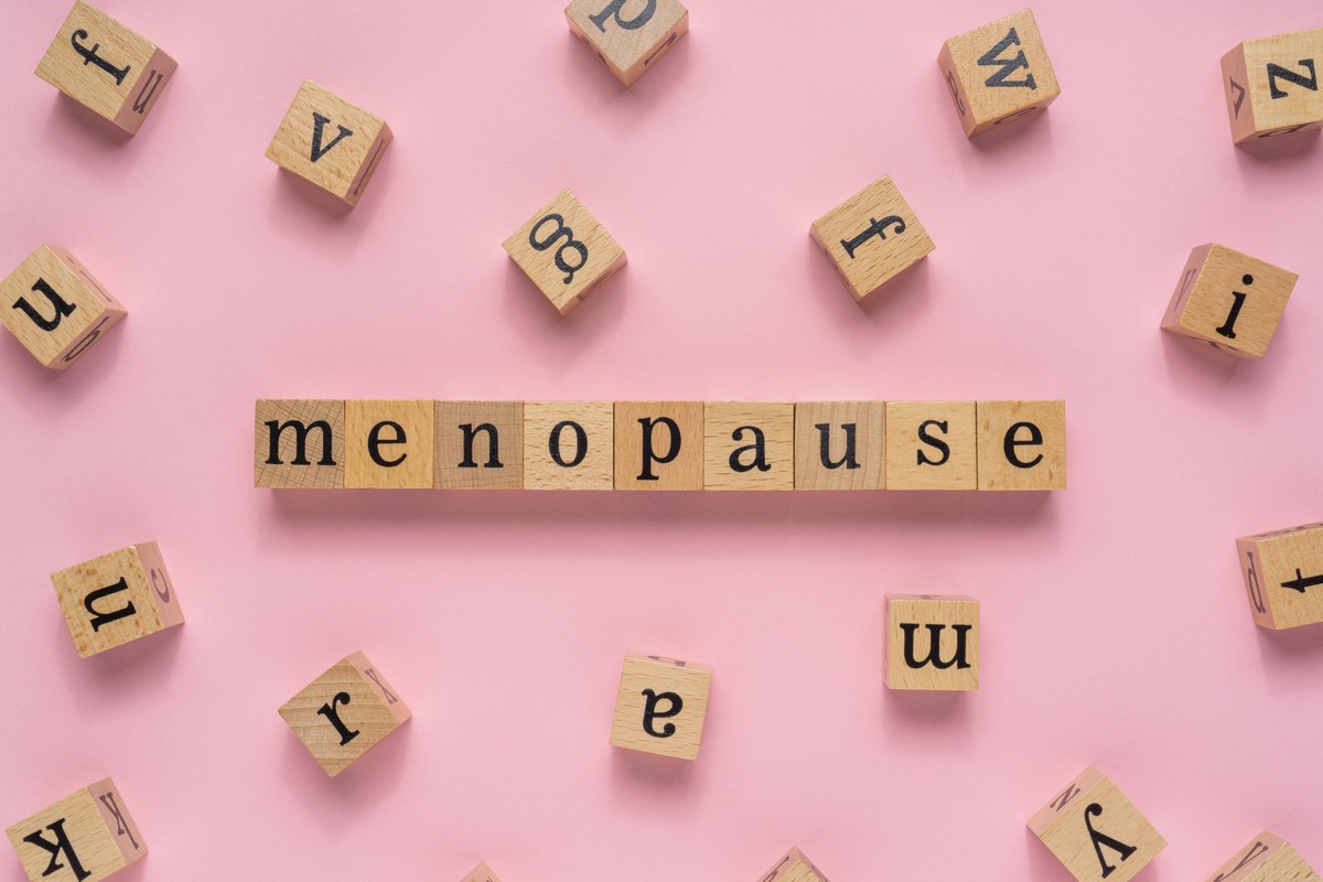 Wooden letter blocks on a pink background spelling out the word 'menopause' with scattered letter blocks around it.