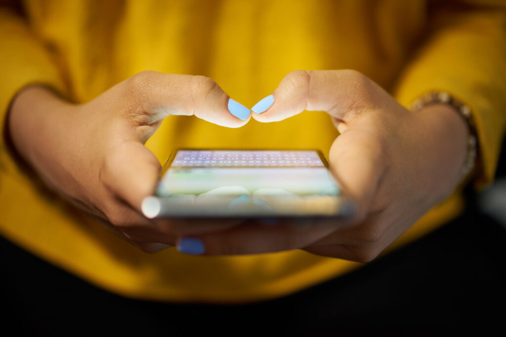 Close-up of a person in a yellow top using a smartphone.