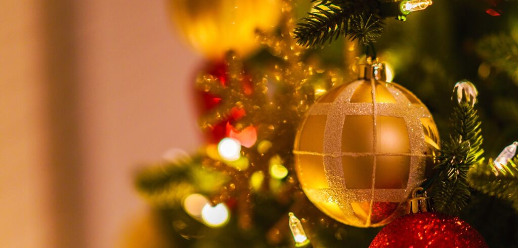 Gold bauble hanging from a Christmas tree among warm lights.