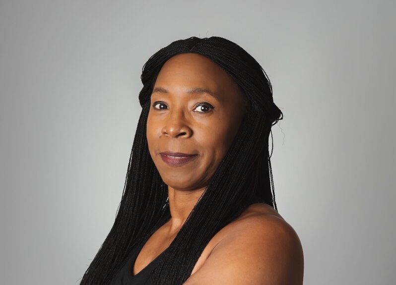 Portrait of a woman with long braids wearing a black sleeveless top.