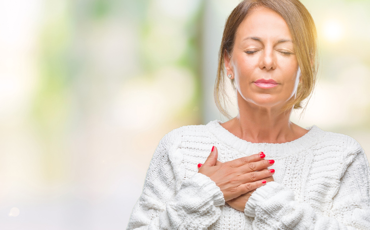 Woman with her eyes closed resting one hand over her chest.