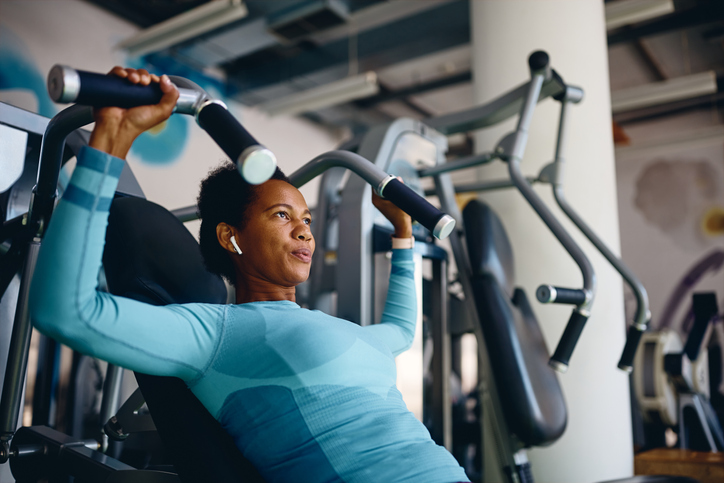 Woman in a turquoise long-sleeved top using a shoulder press machine.
