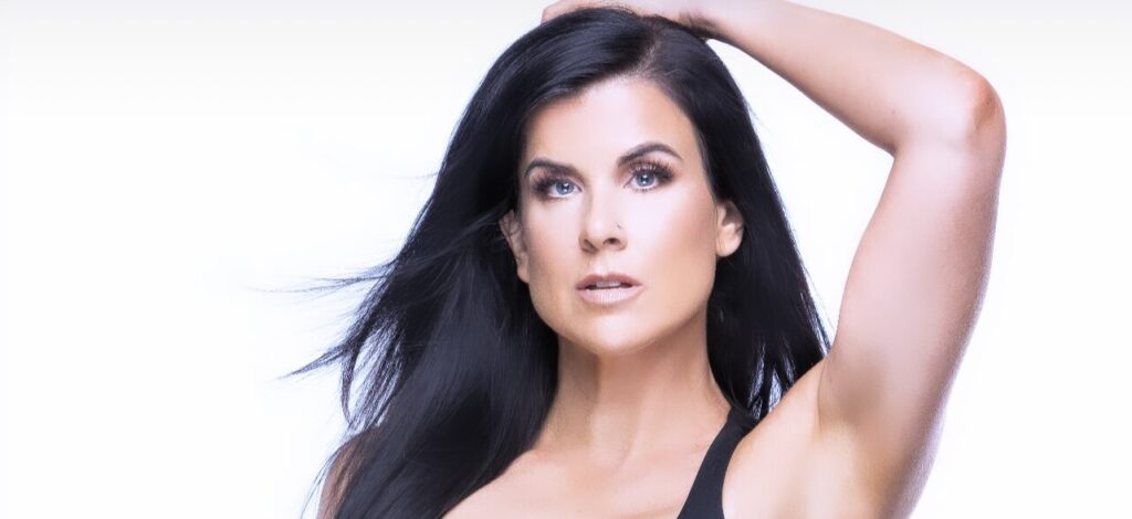 Portrait of a dark-haired woman with one arm raised above her head.