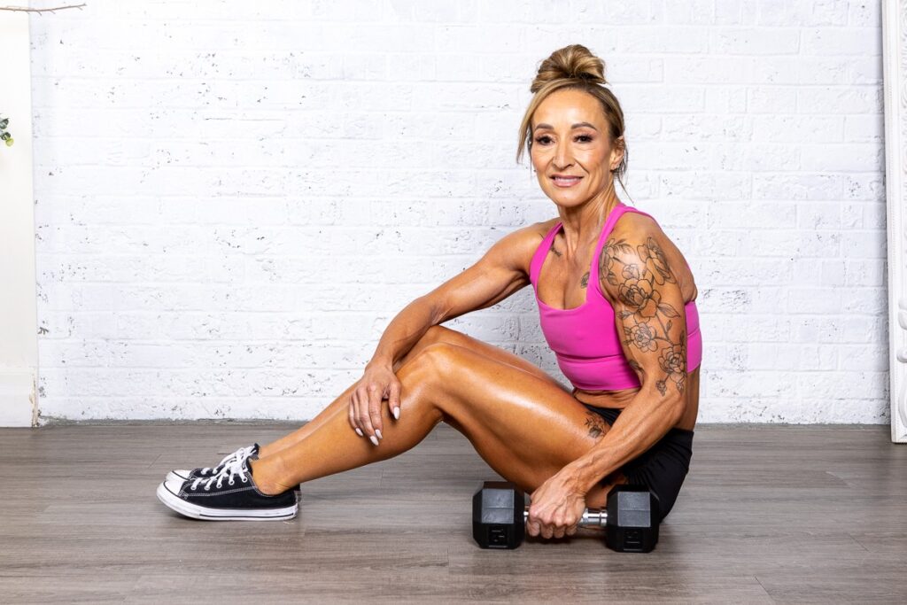 Smiling woman with arm tattoos wearing a pink workout top.