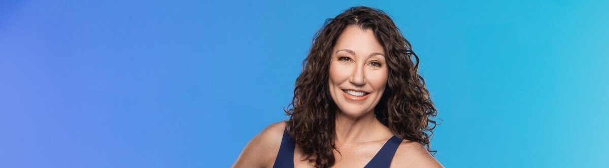 Smiling woman with curly brown hair wearing a dark blue sleeveless top against a blue gradient background.
