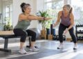 Woman rising from a weight bench with arms extended while another woman observes.
