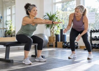 Woman rising from a weight bench with arms extended while another woman observes.