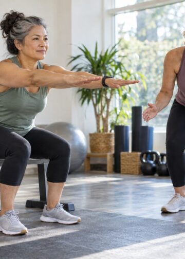 Woman rising from a weight bench with arms extended while another woman observes.