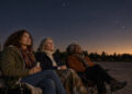 Three midlife women seated in folding chairs looking at a quiet night sky
